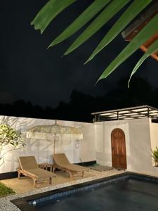 a swimming pool with two chairs and an umbrella at Tri Putri Villa in Badung