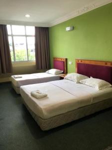 three beds in a room with green walls at Hotel Perdana in Lawas