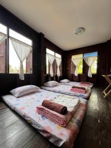 a bedroom with three beds with pillows and windows at The Say Ba Homestay at Mae Chaem เด๊อะเซ่บะ โฮมสเตย์ แม่แจ่ม in Mae Chaem