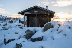 een met sneeuw bedekte hut met zonsondergang op de achtergrond bij Wilderness Hut Lake Tsahkal in Kilpisjärvi