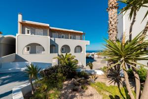 a white house with palm trees and the ocean at Maistros Village Santorini 5 Star in Karterados