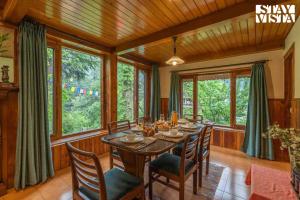 ein Esszimmer mit Tisch und Stühlen und Fenstern in der Unterkunft StayVista at Retreat Cottages with Lawn, Bonfire in Manali