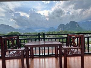 a wooden table and two chairs on a balcony with mountains at Santara Backpackers Hostel in Vang Vieng