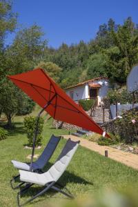 two chairs and a red umbrella in the grass at Magnolias Cottage in Lousã