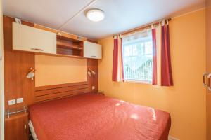 - une chambre avec un lit doté d'un couvre-lit rouge et d'une fenêtre dans l'établissement Mh 25 Les Genêts Ronce les bains, à La Tremblade