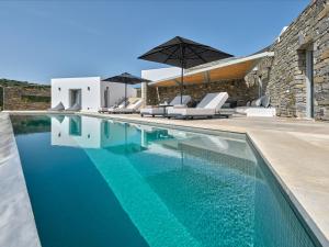 an infinity pool with chairs and an umbrella next to a house at Aegean Hestia Luxury Villa of Paros in Kampos Paros
