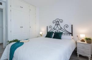 a bedroom with a large white bed with green pillows at Apartamentos Collado Playa Valdelagrana in El Puerto de Santa María