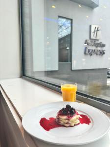 a plate of pancakes with red sauce and a glass of orange juice at Holiday Inn Express Manchester City Centre Arena by IHG in Manchester