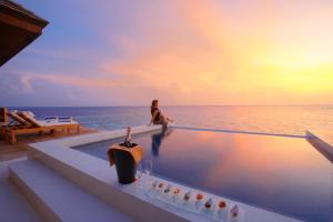 a woman sitting on the edge of a swimming pool overlooking the ocean at Lily Beach Resort and Spa - All Inclusive in Dhangethi