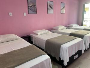 a room with four beds against a pink wall at Pousada Mercosul in Alegrete
