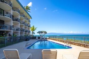 a swimming pool in front of a building with chairs and the ocean at Kahana Reef 120 by Coldwell Banker Island Vacations in Kahana