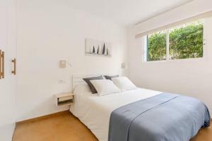 a white bedroom with a large bed and a window at Apartamento Recién reformado con jardín en Arenal de Castell in Es Mercadal