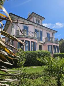 a pink house with blue windows and bushes at Villa Maria Lago Maggiore 2 in Leggiuno