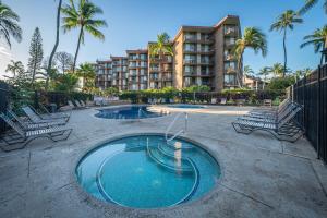 ein Pool mit zwei Stühlen und ein Gebäude in der Unterkunft Kauhale Makai 203 by Coldwell Banker Island Vacations in Kihei