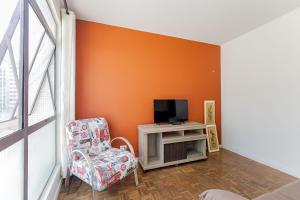 a room with an orange wall and a chair and a tv at Condomínio Edifício Santos Andrade | Gonzaga Stays in Curitiba