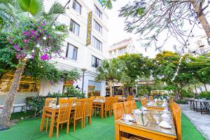 a restaurant with wooden tables and chairs in front of a building at MELANTA HOTEL FLC SẦM SƠN in Sầm Sơn