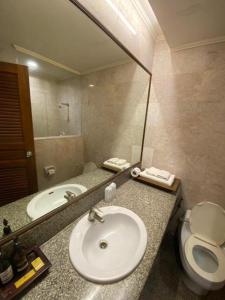 une salle de bain avec un lavabo, des toilettes et un miroir dans l'établissement Sri U-Thong Grand Hotel, à Suphanburi