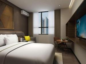 a hotel room with a bed and a desk and a tv at IU Hotel Qingdao Golden Beach Xuejiadao Metro Station in Huangdao