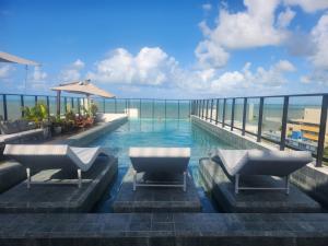 a swimming pool with chairs and the ocean in the background at Loft aconchegante à Beira-Mar in João Pessoa