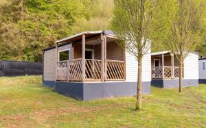 a small house with a porch and a tree at Lodge Camping De la vallée in Durbuy