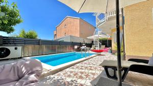 a swimming pool with an umbrella next to a building at Apartman Stipić 2 in Kaštela