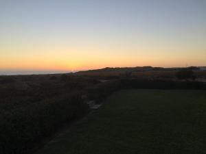 a sunset over a grassy field with the ocean at CASA MILFONTES by Stay in Alentejo in Vila Nova de Milfontes