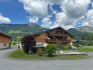 une grande maison en bois avec des montagnes en arrière-plan dans l'établissement Appartement charmant à Morillon, proche du lac et navette, avec terrasse et équipements modernes - FR-1-642-88, à Morillon