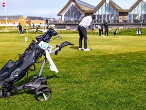 ein Mann, der mit einem Kinderwagen auf einem Golfplatz Golf spielt in der Unterkunft 6 person holiday home on a holiday park in Rømø in Sønderby