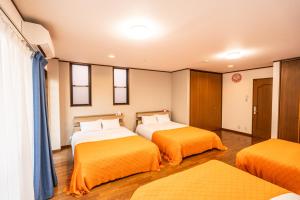 two beds in a room with orange sheets at raikoエレベーター付き大人数向け一棟貸切宿 in Nishi-biwashima