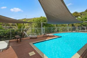 a swimming pool on a deck with chairs and an umbrella at Kaiteriteri Luxury Apartment in Kaiteriteri