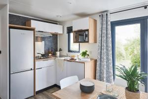 una cucina con mobili bianchi, un tavolo e una finestra di Mobil-Home 6 à 8 personnes ad Ascou