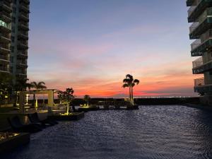 a sunset in a city with palm trees and buildings at Modern 1BR with Balcony Facing Infinity Pool Manila Bay Sunset Near Airports OKADA Solaire MOA in Manila