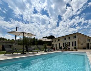 a swimming pool with chairs and umbrellas next to a building at Repaire - Le Repaire de Maltus "Gîtes & Spa" in Lussac