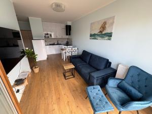 a living room with a blue couch and a kitchen at APARTAMENT BALTICHOFF FUN with Sea View, Basen, Spa, Gym, Sauna, Hala sportowa z kortem tenisowym in Gąski
