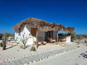 a small house with a thatched roof on the beach at Beheloka Lodge in Ambalaviro