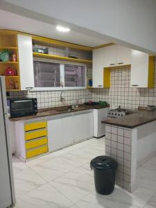 a kitchen with white and yellow cabinets and a black trash can at Suíte Praia Grande in Arraial do Cabo