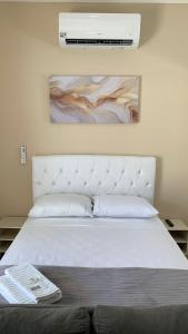 a bedroom with a white bed and a painting on the wall at Quarto Privativo a 3 Minutos do Aeroporto in Sao Jose do Rio Preto