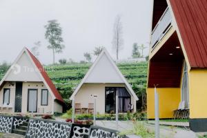 a group of three houses in front of a field at Vianda Cabin By Travelink in Kejajar
