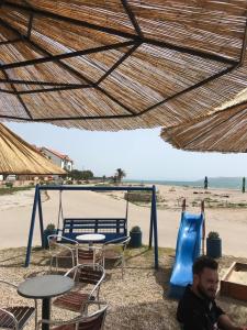 un homme assis sous un parasol de paille à côté d'une aire de jeux dans l'établissement Bella Casa Srima Comfort, à Srima