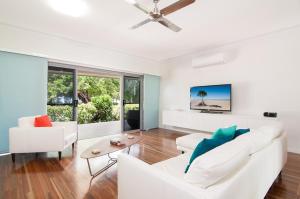a living room with white furniture and a ceiling fan at Jalun Bayun The Sea House in Newell Beach