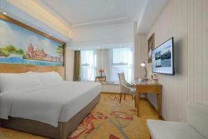 a hotel room with a large white bed and a desk at Vienna Hotel Zhengzhou Only Henan Movie Town in Zhongmou