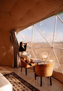 une femme assise sur une chaise dans une pièce avec fenêtre dans l'établissement Olivia Rum Bubbles, à Wadi Rum