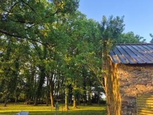 a stone building with a metal roof next to trees at Le petit campîng de Vallye in Maxent