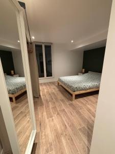 two beds in a room with wooden floors and two windows at Appartement chez maison hôte rez de jardin in Charmeil