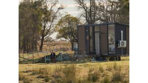 a woman sitting on a bench in front of a tiny house at Little Argyle Tiny House by Tiny Away in Coonabarabran