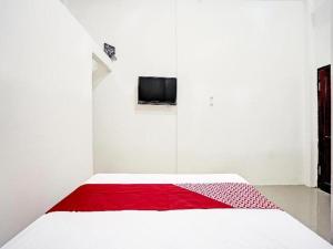 Cette chambre blanche comprend un lit avec une couverture rouge. dans l'établissement Hotel O Grand Syariah Hagawa Lamongan Near SPORT CENTER LAMONGAN, à Lamongan