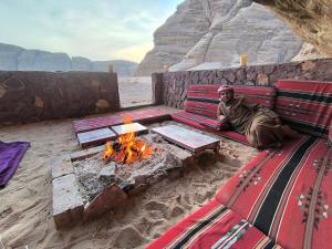 a man sitting on a couch next to a fire pit at Wadi Rum Desert Experience in Wadi Rum