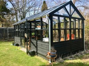 a black greenhouse in the grass in a yard at Cozy summer cottage with orangery close to Heatherhill and Beach in Vejby