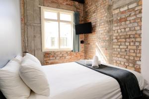 Un dormitorio con una cama blanca con una pared de ladrillo. en Haka House Auckland K'Road, en Auckland