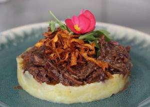a piece of food with meat on a plate with a flower at Hôtel - Restaurant U Santu Petru in Saint-Florent